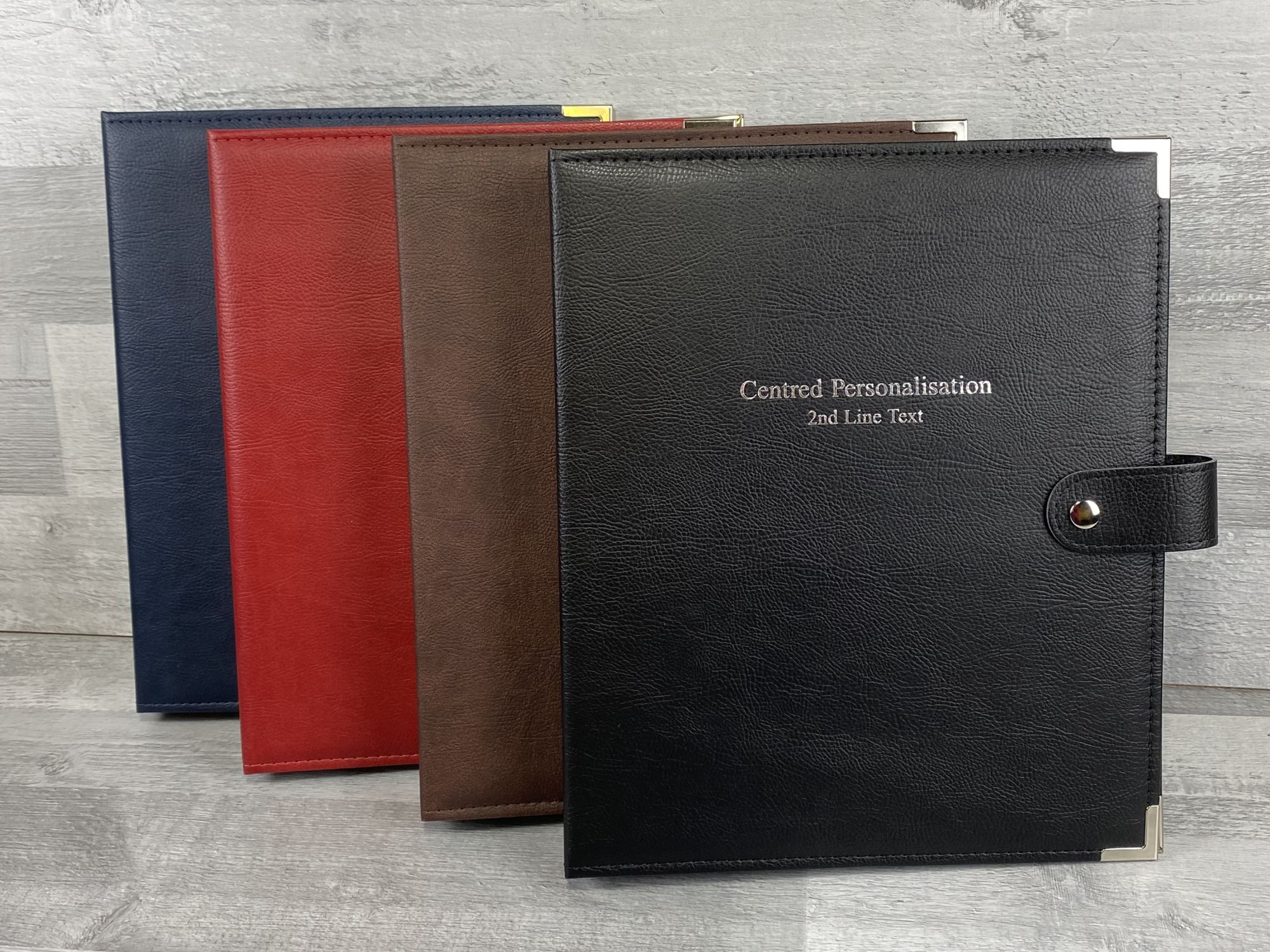 four faux leather ring binders and ring folders in colours red, blue, black and brown. black ring binder has centred personalisation in silver foil on front cover